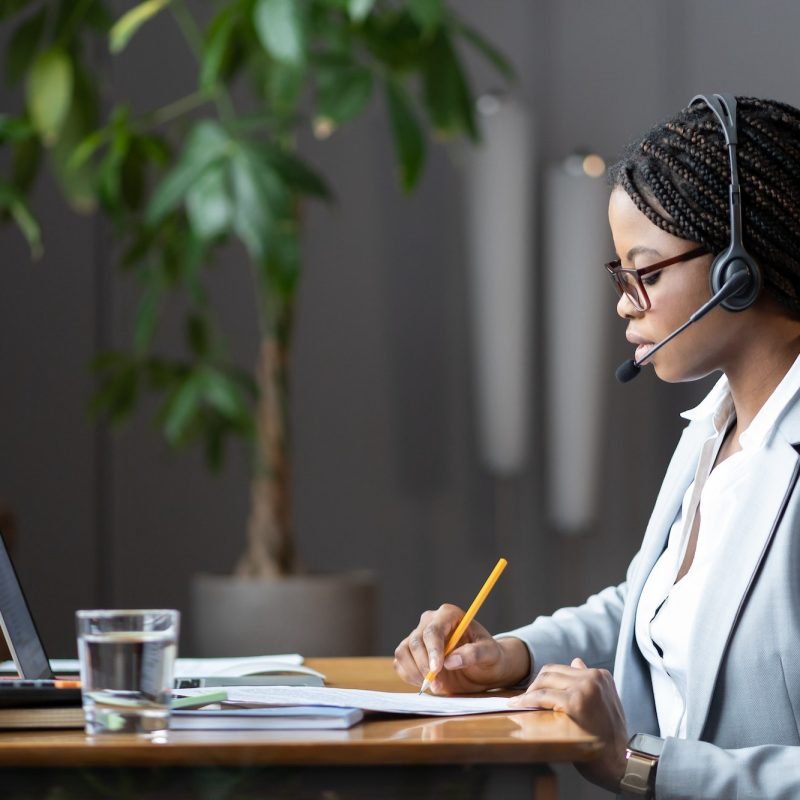 focused-african-female-home-based-virtual-assistant-in-headset-making-notes-during-online-meeting.jpg